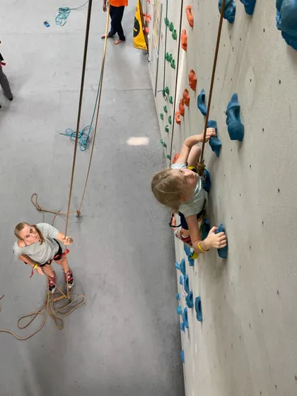 An overhead view of two young climbers, one on the wall and one belaying. We teach kids to be responsible and supportive climbing partners.