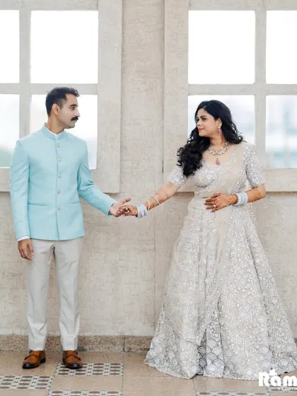 A clean and elegant portrait against a simple, bright background. The groom leading the bride by the hand creates a sense of a new journey beginning, with their coordinated pastel outfits adding to the soft aesthetic.