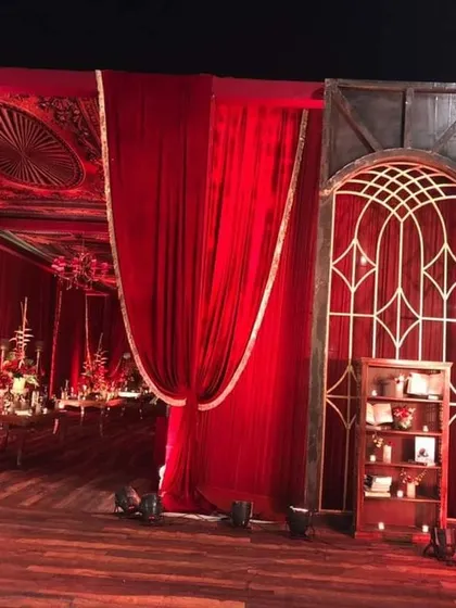 A closer look at the details of the royal red wedding entrance. The arched window frame and bookshelf filled with candles and books add a unique, vintage library theme to the opulent decor, creating interesting corners for guests to discover.