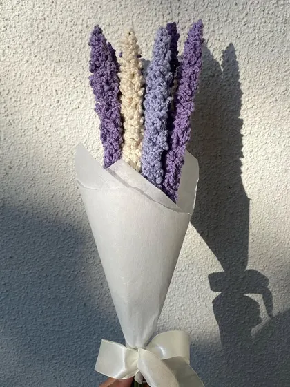 A lovely bouquet of handmade crochet lavender in different shades of purple and cream. The simple white paper wrapping and ribbon highlight the natural, rustic beauty of the flowers.