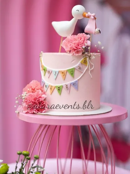 A sweet and simple cake for a Paris-themed baby shower. The pink cake is topped with a stork carrying a baby, and a mini bunting, perfectly capturing the "Bonjour Bébé" theme.