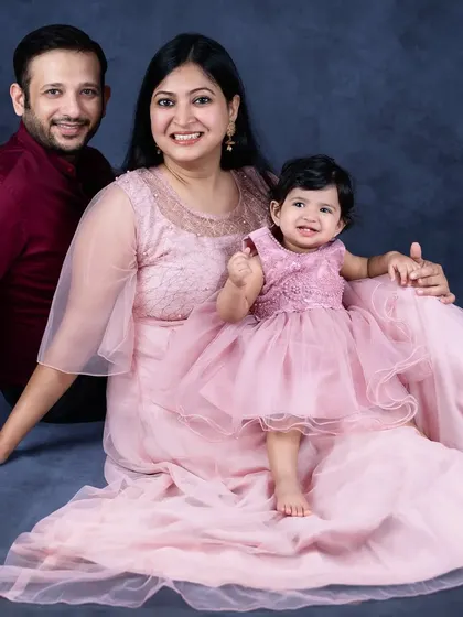 A family of three in coordinated pink outfits. The baby girl sits on her mother's lap, creating a lovely and harmonious family photo.