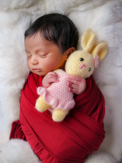 Pure innocence. A simple red swaddle and a fluffy white background are all that's needed to create a striking and beautiful portrait of this sleeping baby.