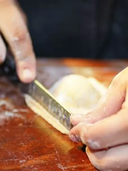 The precise art of hand-cutting fresh pasta dough. This action shot emphasizes the hands-on, artisanal approach we take at our live Italian cooking stations.