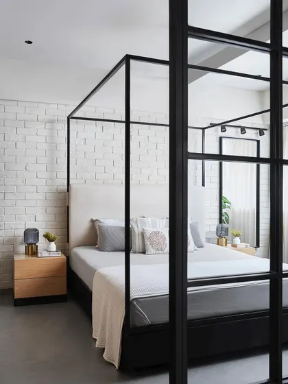 A view of the Zen House bedroom as seen through the black-framed glass partition of the study. This design choice connects the two spaces visually while providing acoustic separation.