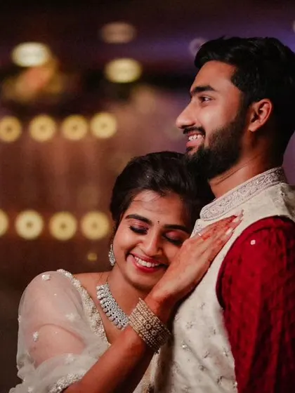 An intimate reception photo with beautiful bokeh lighting in the background. The bride's happy expression as she leans on her groom makes this a warm and romantic shot.