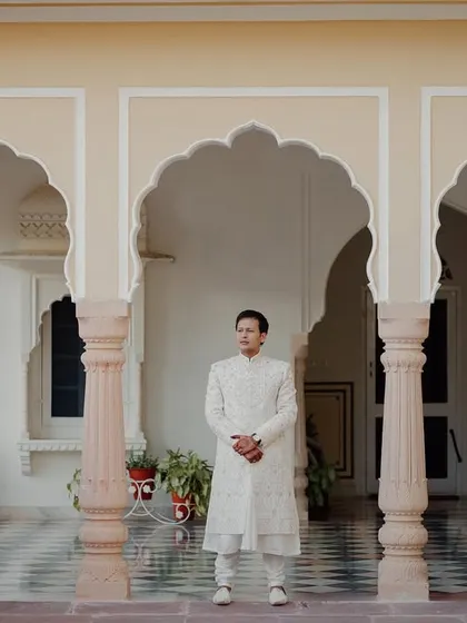A classic groom portrait in a royal setting, with the groom standing in a corridor of ornate pillars and arches.