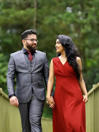 A modern pre-wedding shoot with the couple in stylish western outfits, walking across a bridge in a park.
