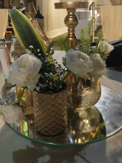 A close-up of a tabletop centerpiece, featuring delicate white roses in a textured golden vase, reflecting the understated luxury of the Sufi-themed event.