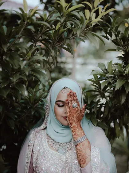 The bride's eyes are closed in a moment of serenity, her henna-adorned hand creating a beautiful and artistic pose.