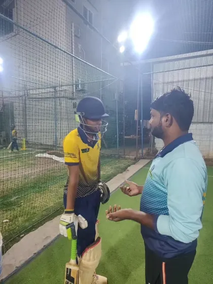A coach provides feedback to a young batsman during a night session. This individual attention is crucial for making small technical adjustments that lead to big improvements.