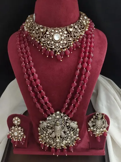 This Victorian-style jewellery set features deep red beads and an antique finish. The pendant showcases a traditional Krishna motif, blending different styles beautifully.