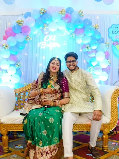 A lovely portrait of the expecting couple seated on a comfortable couch at their baby shower, surrounded by a blue and pink balloon arch.