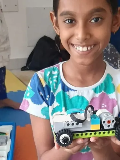 A smiling student holds up her completed robotic car, a testament to the hands-on learning and fun at our camps.