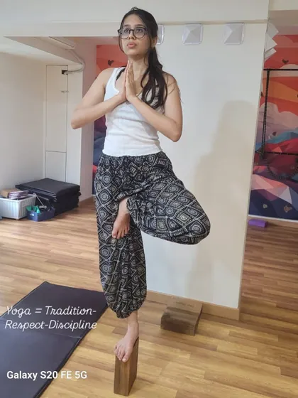 A yoga block is used here to challenge and refine balance in Vrikshasana (Tree Pose). Practicing on an unstable surface like a block strengthens the small muscles in the feet and ankles, improving overall stability and focus.