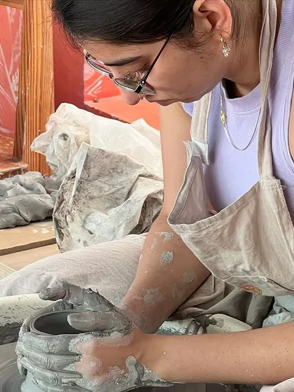 A student completely in the zone, focused on shaping her piece on the wheel. It's a very meditative and calming process.