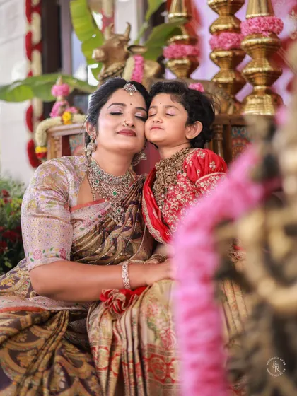 A mother and child share a tender, eyes-closed moment of affection amidst the backdrop of a traditional ceremony.