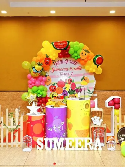 A bright and healthy "Tutti Frutti" theme. This colorful setup uses fruit-themed props and a vibrant balloon garland, offering a fun and unique alternative to character themes.