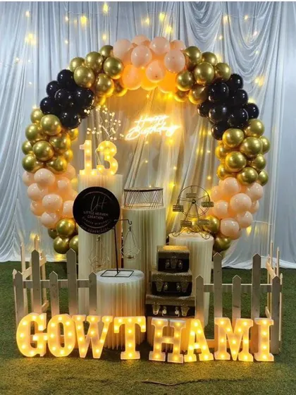 A glamorous 13th birthday party with a black, gold, and peach balloon arch. The outdoor setup includes a picket fence and large marquee letters.