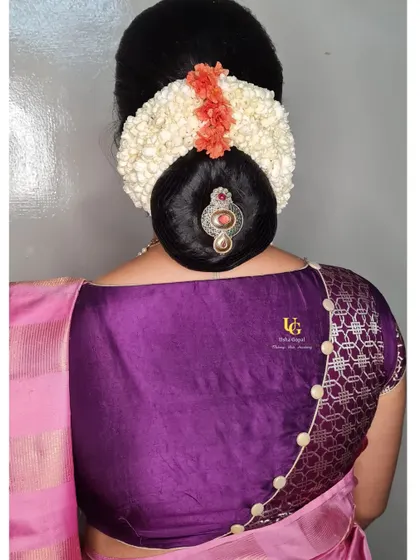 An elegant and timeless floral bun hairstyle. This classic look features a neat bun adorned with fresh jasmine (gajra), orange crossandra (kanakambaram), and a traditional bun accessory.