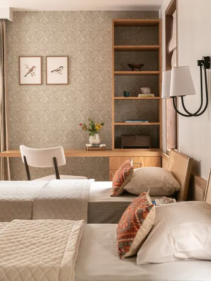 The guest room features a cozy study nook with a beautiful bird-patterned wallpaper. The light wood tones and soft textiles create a pared-down yet warm and welcoming vibe.