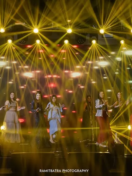 A dramatic shot of the bridesmaids performing on a stage filled with stunning light beams at a Sangeet night in Goa.