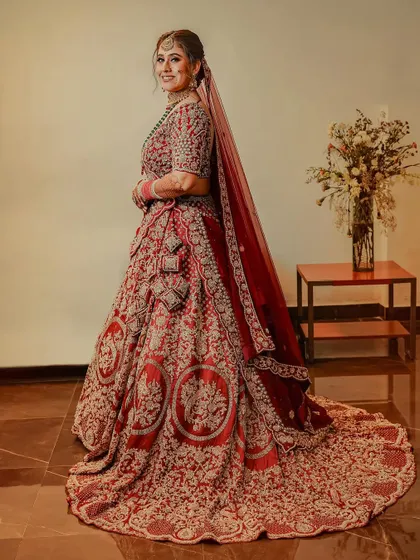 A full-length portrait of the bride, showcasing the magnificent train of her red and gold lehenga. Her happy smile and confident pose complete this beautiful bridal shot.