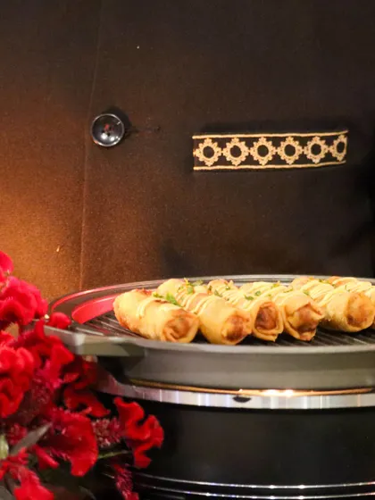 A tray of crispy spring rolls, presented by a server in our elegant uniform. The close-up shot highlights the perfect golden-brown texture of the rolls and the professionalism of our staff.