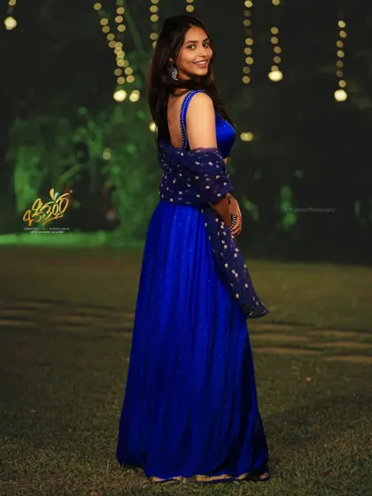 A side-profile portrait of actress Sapthami Gowda against a backdrop of festive lights. The composition and lighting create a graceful and eye-catching image.