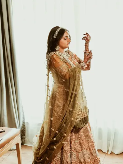 A full-length shot of the bride, Maitri, as she gets ready. The natural light from the window beautifully illuminates her pastel lehenga.
