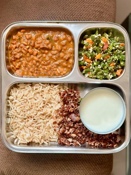 This vegetarian thali includes brown rice, black-eyed pea curry, horse gram sundal, sautéed beans, and curd.