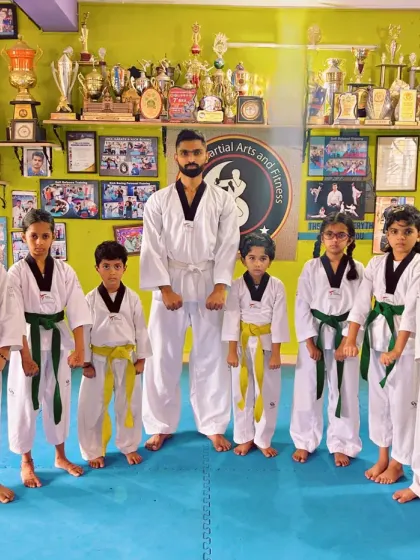 Our Taekwondo India team in their doboks, standing ready and disciplined in front of our academy's wall of trophies.