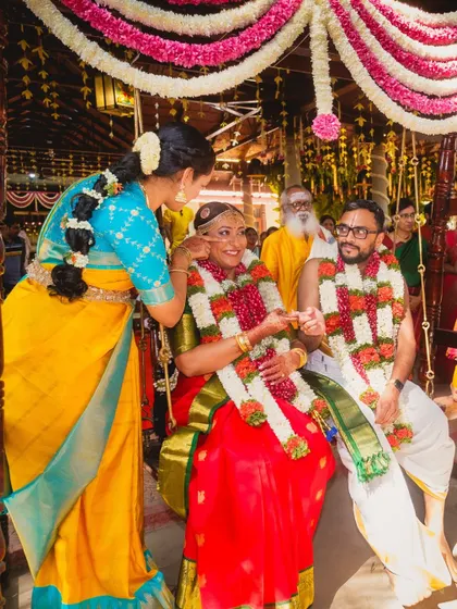 A bridesmaid helping the bride during a traditional Tamil Brahmin wedding ceremony, her own vibrant Kanjeevaram saree perfectly complementing the scene.