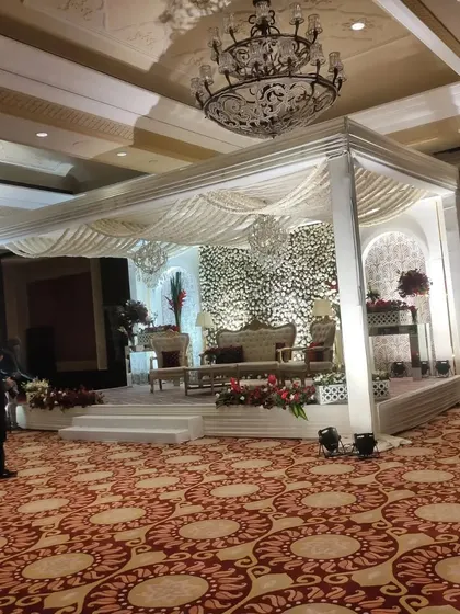 This is an example of a luxurious indoor reception stage setup in a hotel banquet hall. I designed a grand white canopy with a full floral backdrop, elegant seating for the couple, and professional lighting to create a sophisticated and picture perfect setting.