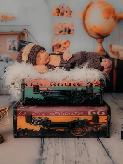 A full-length view of the sleeping baby on the suitcases. This shot effectively showcases the scale and artistry of the entire themed newborn setup.