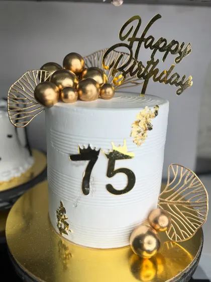 A chic and modern cake for a 75th birthday. The design is minimalist yet elegant, with golden spheres, leaf accents, and gold foil, perfect for a stylish celebration.