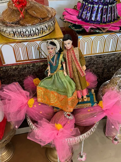 A close-up of a couple doll arrangement for a wedding platter. The dolls are dressed in detailed traditional outfits and placed on a beautifully decorated base with pink tulle.