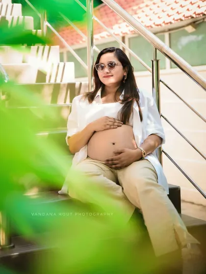 A modern and stylish maternity shot of a mother-to-be baring her bump, sitting casually on outdoor stairs. This shows a more contemporary approach to pregnancy portraits.