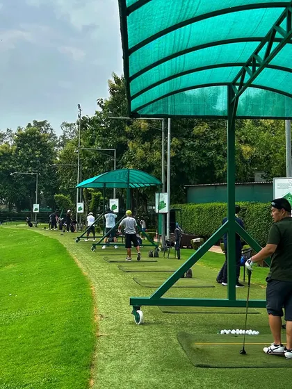 A golfer stands ready at his bay, with the long line of the driving range stretching out ahead.