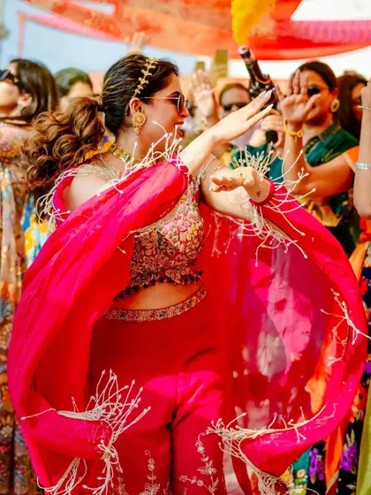 The bride twirling in her vibrant pink outfit, her fringed cape creating beautiful movement as she dances at her Haldi.