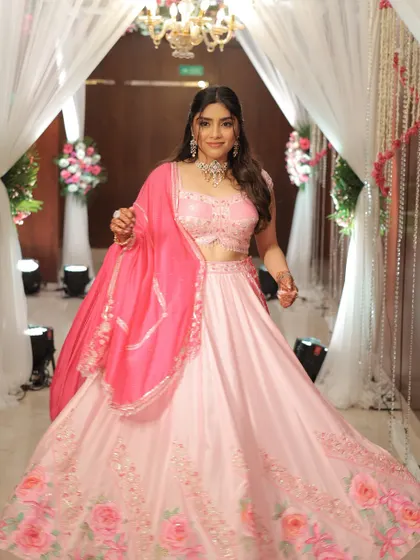 A full view of this stunning engagement look. The pink floral lehenga is perfectly complemented by flushed cheeks, glossy lips, and a half-up hairstyle with soft curls for a romantic finish.