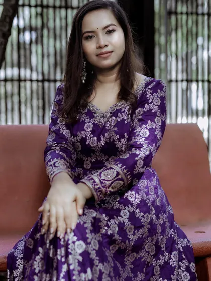 A seated pose in the purple brocade Anarkali, highlighting the rich fabric and intricate design.