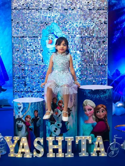 A spectacular Disney Frozen theme for a 5th birthday celebration. The entire venue was transformed into a winter wonderland with shades of blue and silver, a sequin backdrop, and life-sized cutouts of Elsa, Anna, and Olaf.