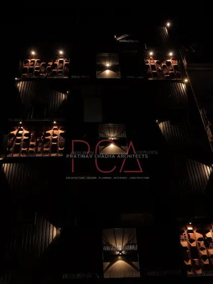 A dramatic night shot of the Chadha Properties office facade, with uplighting emphasizing the texture of the terracotta jaalis.