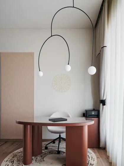 This bedroom in a Mumbai home features a modern, minimalist aesthetic. A simple terracotta-colored desk is paired with an elegant arched pendant light, creating a clean and inspiring workspace within the room.