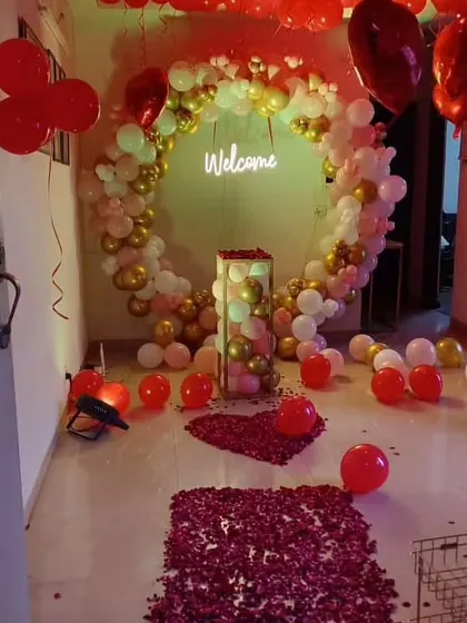 A grand welcome setup featuring a large circular balloon arch in white and gold. The entrance path is decorated with rose petals, leading to a 'Welcome' neon sign inside the arch.