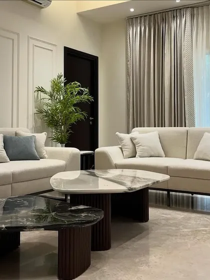 Another angle of this elegant living room, highlighting the sleek metal legs of the sofas and the rich, dark wood of the fluted table bases. It's a study in contrasting materials and textures.