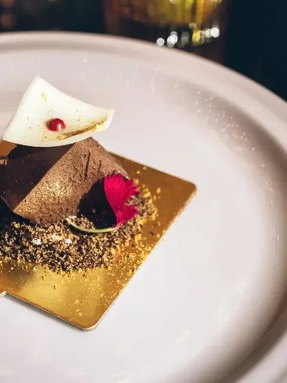 Our Belgian Dark Chocolate Mousse, elegantly plated on a gold square with an edible flower.