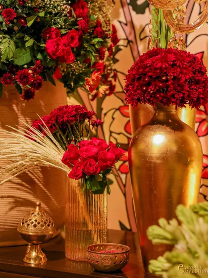 A close-up of the decor details, showing rich red flowers in golden vases alongside a traditional incense burner. Every element is chosen to evoke the sensory experience of a spiritual and festive gathering.