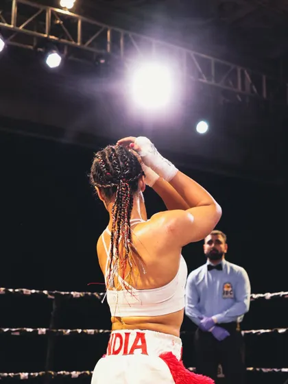 Pure, unfiltered passion. A female fighter ties her hair, focused and ready for battle under the bright lights.